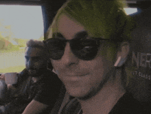 a man with green hair wearing sunglasses sits next to another man with a beard