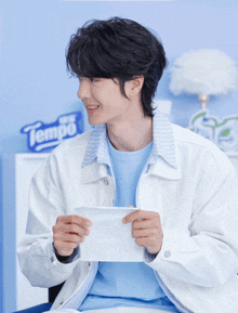 a man in a white jacket holds a piece of paper in front of a sign that says tempo