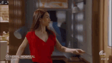 a woman in a red shirt is standing in front of a door that says general hospital weekdays on it .