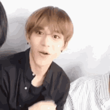 a young man in a black shirt is sitting next to another young man in a striped shirt .