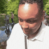 a man in a white shirt stands in front of a pond