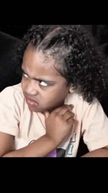 a little girl with curly hair is making a funny face while sitting down .