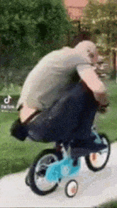 a man is riding a small bicycle with training wheels on a sidewalk .