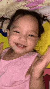 a little girl in a pink tank top is smiling and waving