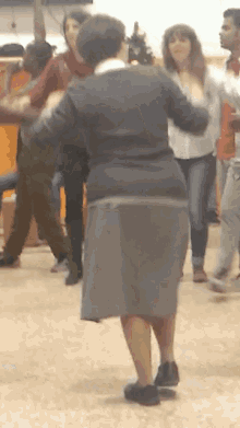 a woman in a gray skirt is dancing in a room with other people