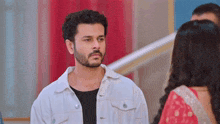 a man with a beard is wearing a white jacket and looking at a woman in a red dress .