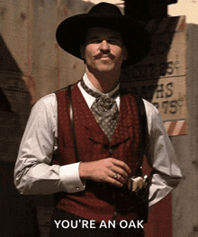a man in a cowboy hat and vest is standing in front of a sign that says " you 're an oak "