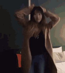 a woman in a long coat is dancing in a room with a bed .