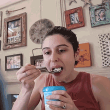 a woman in a red tank top with the letter e on it is eating a spoonful of food