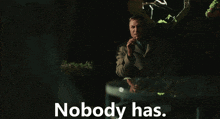 a man sitting at a table with the words " nobody has " behind him