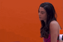 a woman is sitting in front of an orange wall and looking down .