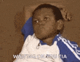 a young boy in a blue and white shirt is sitting on a couch with his hands behind his head .