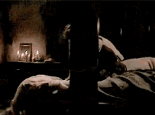 a woman in a white dress is laying on the floor in a dark room with candles in the background