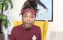 a man wearing a headband and a maroon vans shirt is sitting in a yellow chair