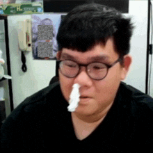 a man with glasses and a napkin in his nose looks at the camera