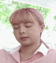 a close up of a woman 's face with her eyes closed . she is wearing a pink and white striped shirt .