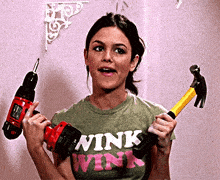 a woman wearing a wink shirt holds a drill and hammer