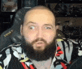 a bald man with a beard is sitting in front of a microphone making a funny face .