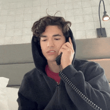 a young man in a black hoodie is talking on a phone