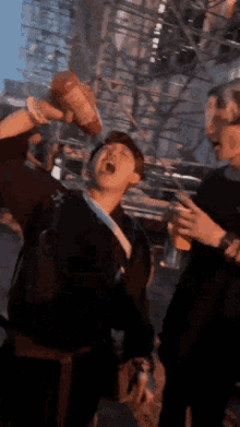 a man is drinking ketchup from a bottle while another man holds a glass