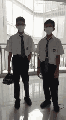 two boys wearing masks stand next to each other in front of a window