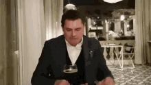 a man in a suit and tie is sitting at a table with a glass of wine .