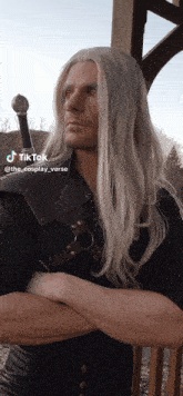 a man with long white hair is standing with his arms crossed and a sword in his hand