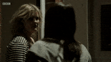 a woman looks at herself in a mirror with the bbc logo on the bottom right