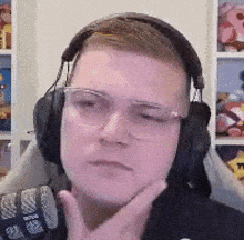 a man wearing headphones and glasses is sitting in front of a microphone with his hand on his chin .