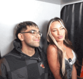 a man and a woman are posing for a picture and the man is wearing glasses and the woman is wearing a bra