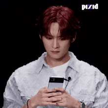 a man with red hair is holding a cell phone in his hands and looking at it .