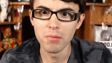a man wearing glasses is making a funny face in front of a shelf with dolls on it