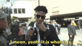 a man talking into a microphone with the words " i mean yeah it is what it is " above him