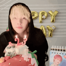 a man in a black hoodie is holding a birthday cake with candles that say 23 on it