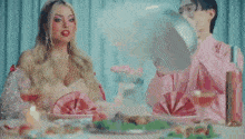 a woman in a pink dress is sitting at a table with a man in a pink shirt smoking a cigarette .