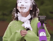 a woman with foam on her face is holding a purple gun .