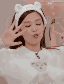 a girl wearing a white headband with ears is smiling and waving