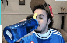 a man wearing a blue shirt and a hat is drinking from a blue bottle