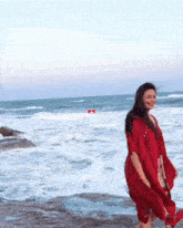 a woman in a red dress stands on the beach