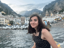 a woman is standing in front of a body of water with mountains in the background
