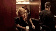 a woman is standing in a room holding a cup of coffee while another woman stands behind her .