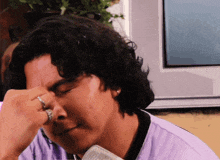 a man with curly hair and a ring on his finger wipes his forehead