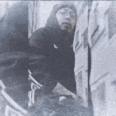 a man in a black hoodie is standing next to a building .