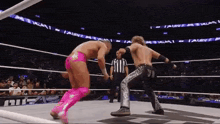two wrestlers are fighting in a wrestling ring with a referee watching .