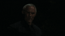 a man with gray hair and a beard is looking at the camera in the dark .