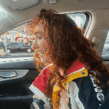 a woman with curly hair is sitting in a car wearing a jacket that says ' abercrombie ' on it
