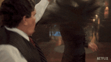a woman in a black dress is dancing with a man in a suit and tie in front of a netflix logo