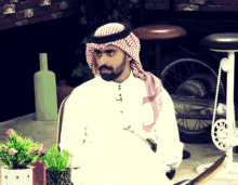 a man wearing a head scarf and a white shirt sits in front of a bicycle wheel