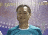 a man in a blue shirt is smiling while standing in front of a wall .