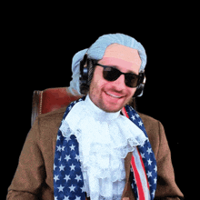 a man wearing a wig and sunglasses is sitting in a chair with an american flag around his neck